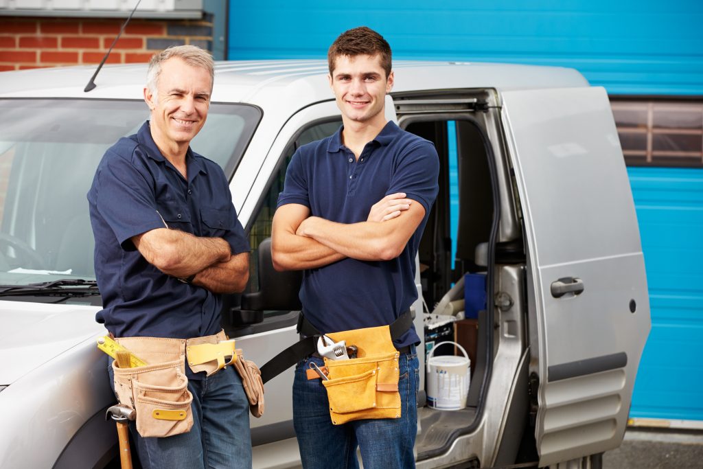 two plumbers standing next to their plumbing van outside of a home after sewer repair